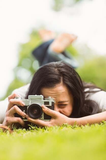 Brunette lying on grass with retro camera taking picture