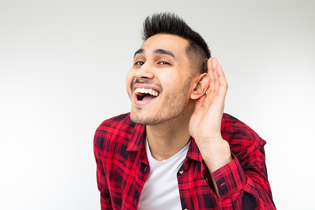 Brunette man in a checkered shirt wide open eavesdrops on a conversation on a white studio background.