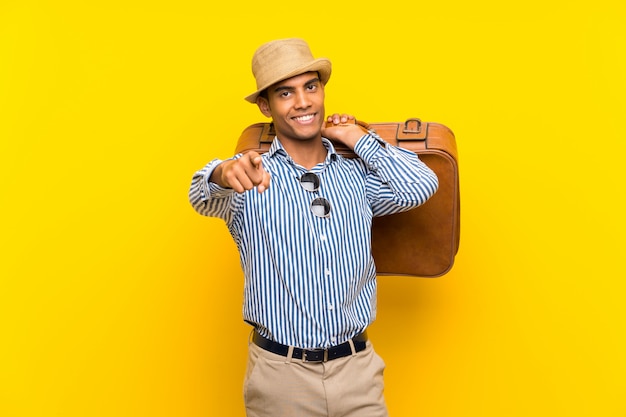 Brunette man holding a vintage briefcase over isolated yellow background surprised and pointing front