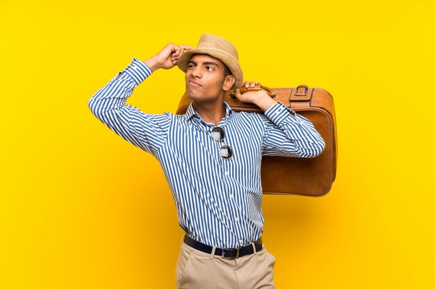 Brunette man holding a vintage briefcase over isolated yellow wall having doubts and with confuse face expression