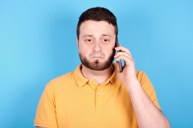 Brunette man using mobile phone and scared. Isolated on blue background.