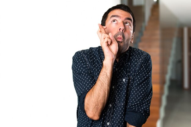 Brunette man with his fingers crossing inside house