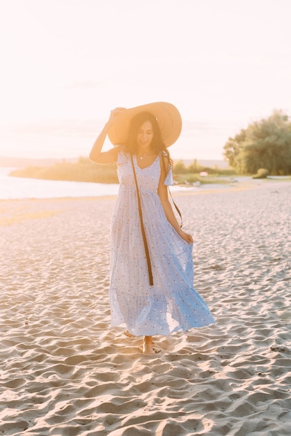 brunette meisje in een elegante zomeroutfit en strohoed in de stralen van de zon op natuurwandeling