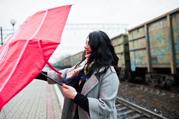 Brunette meisje in grijze jas met rode paraplu in treinstation