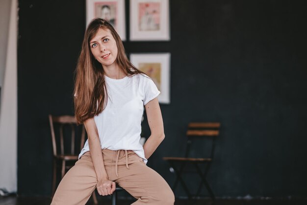 brunette meisje met gekleed in witte t-shirt en jeans zittend op de stoel op de zwarte achtergrond