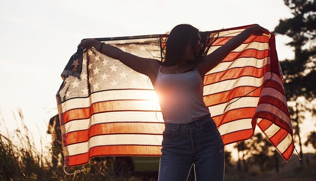 Brunette met Amerikaanse vlag in handen heeft een goede tijd en voelt zich buiten op zonnige dag vrij freedom