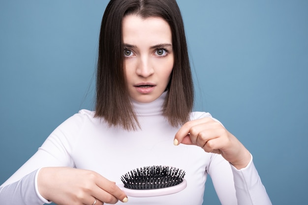 Foto brunette met een kam in haar handen in shock van haaruitval. studio portret blauwe achtergrond.