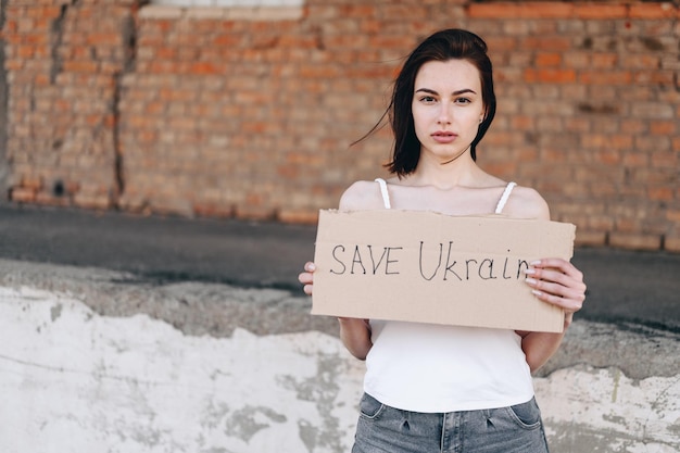 Brunette met kort kapsel met poster in haar handen save oekraïne haar ontwikkelt zich tegen de wind