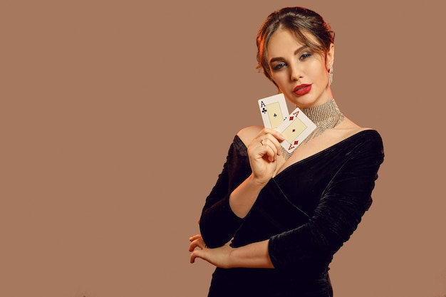 Brunette model, blote schouders, in zwarte jurk en sieraden. het tonen van twee speelkaarten, die zich voordeed op bruine achtergrond. poker, casino. detailopname