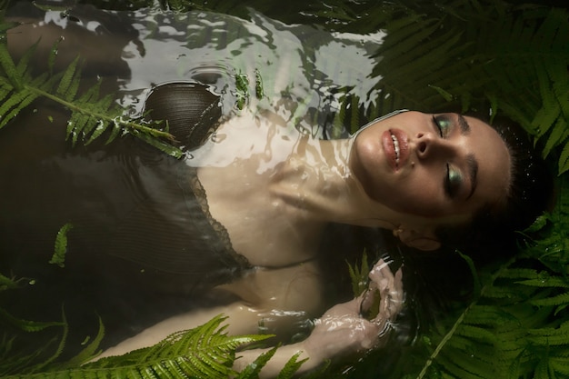 Brunette model in bodysuit in black bath with fern