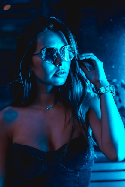 Brunette model 's nachts in de stad met blauwe leds blauwe bril en een horloge kijkend naar de camera