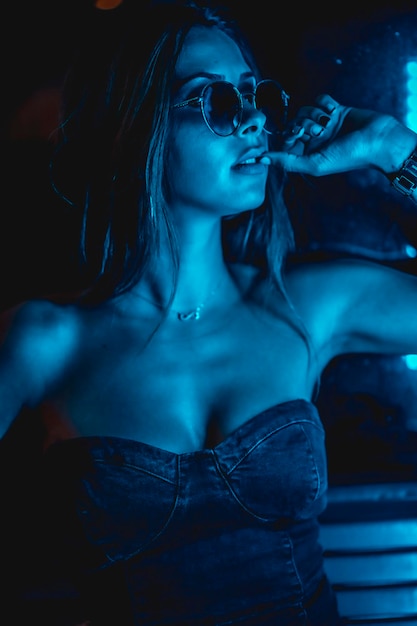 Brunette model 's nachts in de stad met blauwe leds blauwe bril in een donker glas met een verleidelijke look
