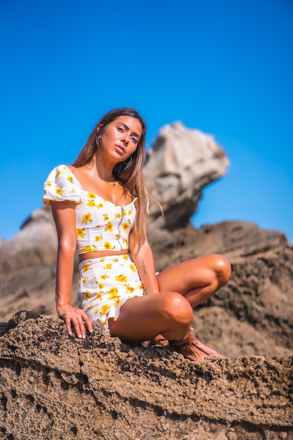 Brunette model in a white dress on the beach enjoying the summer sitting on some rocks