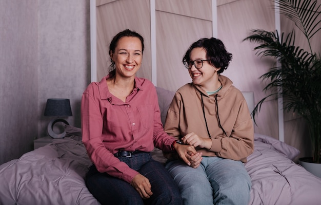 Brunette moeder en tienerdochter zitten op het bed in de kamer en lachen