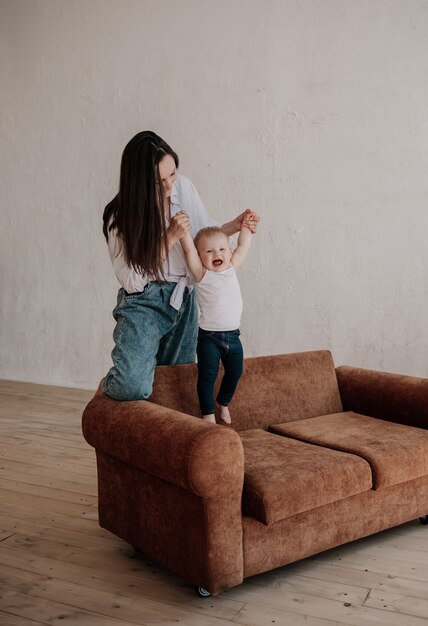 Brunette mom plays with her little daughter on a brown sofa