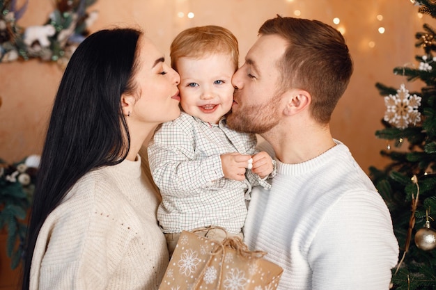 Brunette mother father and little son standing near Christmas tree and hugging