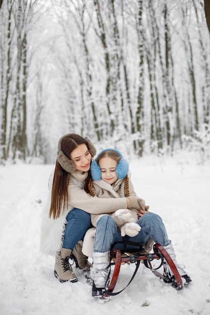 Brunette mother and and her daughter riding a sled in winter forest