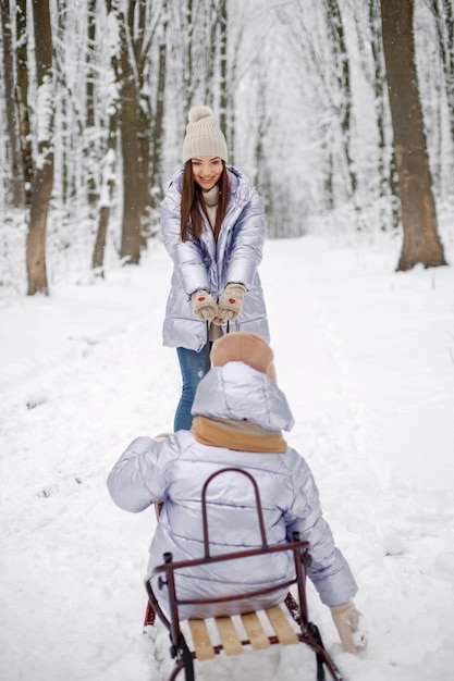 Brunette mother and and her daughter riding a sled in winter forest