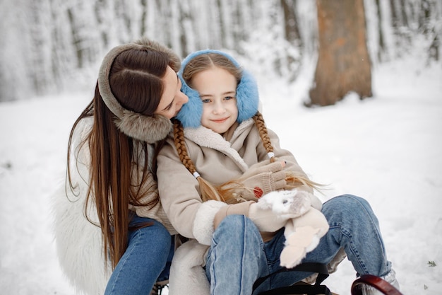 Brunette mother and and her daughter sitting on a sled in winter forest