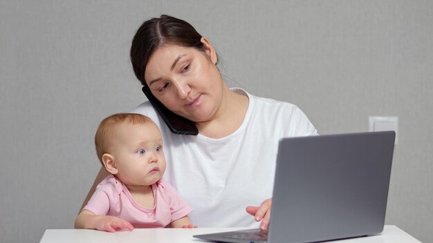 Brunette mother talks with colleague on phone holding baby