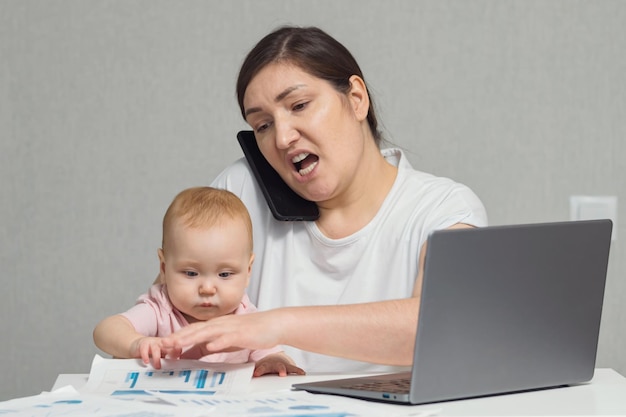 Brunette mother talks with colleague on phone holding baby