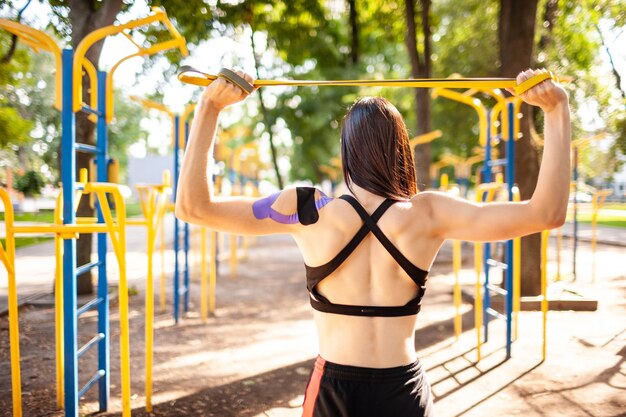 Brunette muscular woman posing with fitness resistance band in park