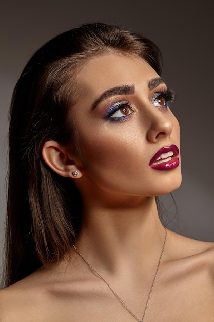 Brunette naked female in jewelry posing on gray background colorful eyeshadow false eyelashes glossy...