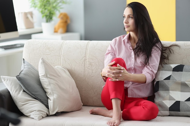 Brunette pensive young woman looking away sitting on couch at home