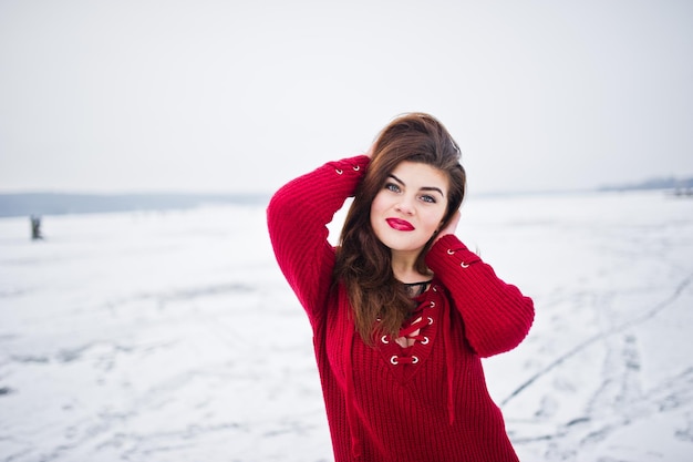 Brunette plus size model at red against frozen lake on winter day.