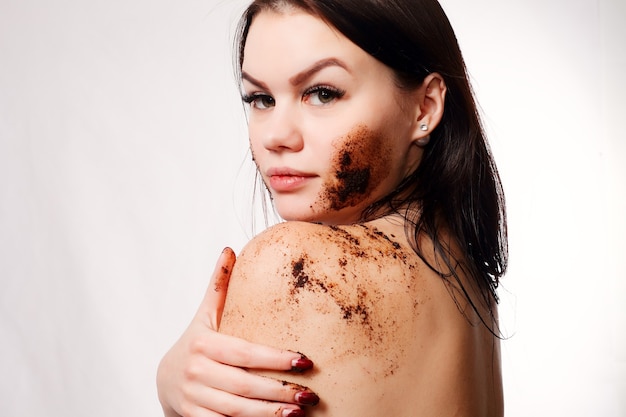 Brunette reinigt huid koffie scrub witte muur.