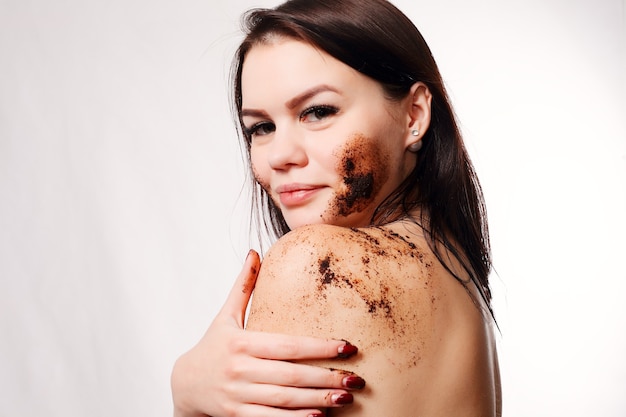 Brunette reinigt huid koffie scrub witte muur.