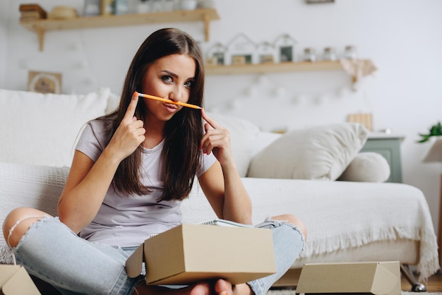 brunette sits on floor near the sofa and twisting her lips with a tube holds a pencil near her lips