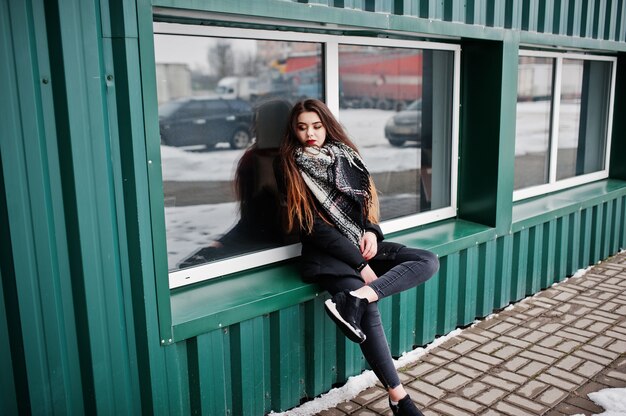 Brunette stylish casual girl in scarf against green metallic wall.