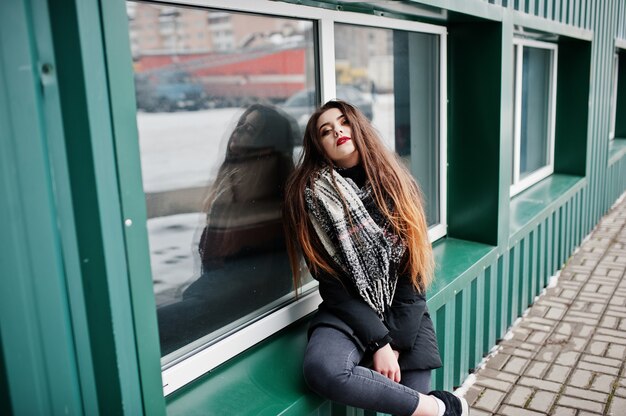 Brunette stylish casual girl in scarf against green metallic wall.