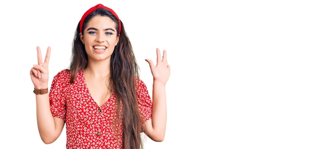 Брюнетка-подросток в летнем платье показывает и указывает пальцами номер семь, улыбаясь уверенно и счастливо