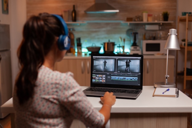 Brunette video-editor werkt 's nachts met beelden op persoonlijke laptop in de keuken thuis home