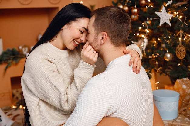 Brunette vrouw en bebaarde man zitten in de buurt van de kerstboom en knuffelen