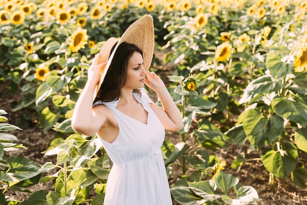 brunette vrouw in een elegante zomeroutfit en strohoed in de zonnestralen tijdens een natuurwandeling