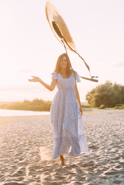 brunette vrouw in een elegante zomeroutfit en strohoed in de zonnestralen tijdens een natuurwandeling