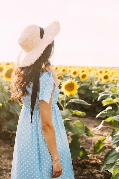 brunette vrouw in een elegante zomeroutfit en strohoed in de zonnestralen tijdens een natuurwandeling