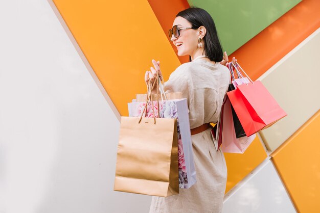 Brunette vrouw met boodschappentassen poseren op de gekleurde muur van de winkel