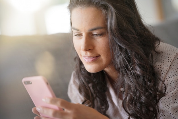 Brunette vrouw ontspannen op de sofa, verbonden met smartphone