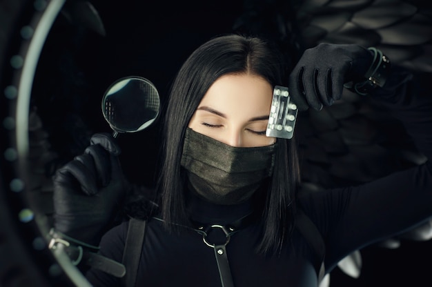 Brunette wearing a protective black coronavirus mask with pills and a magnifying glass