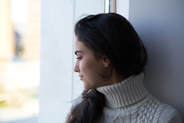 Brunette in a white sweater looks out the window