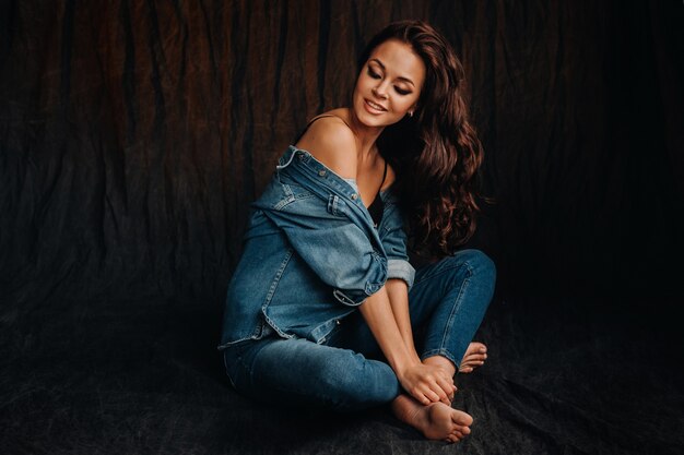 a brunette with long hair poses sitting on the floor