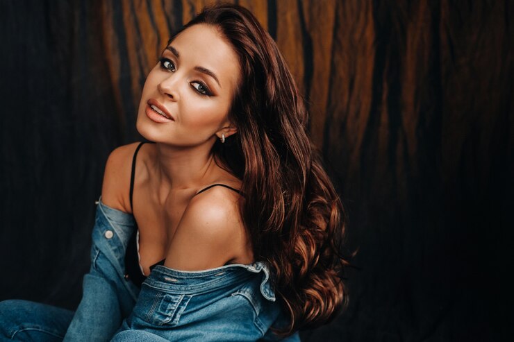 Photo a brunette with long hair poses in a studio sitting on the floor on a black background.