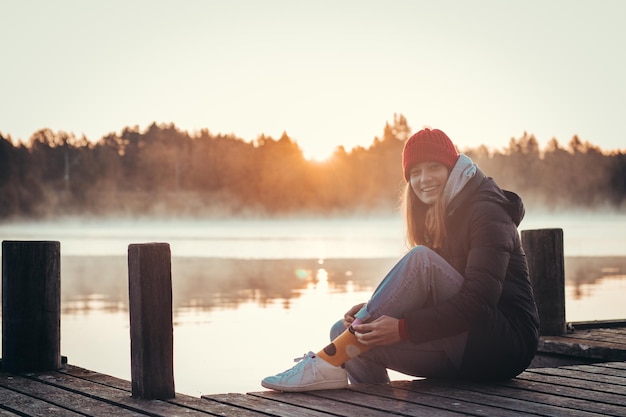 写真 リアルな微笑みを浮かべた黒人女性が日の出時に湖のほとりにある木製の橋の上に座っていますパルタモフィンランド