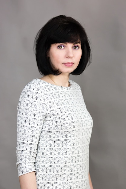 Brunette woman 40 years old in a gray dress on a gray background.