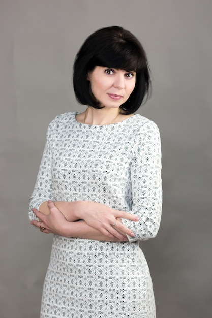 Brunette woman 40 years old in a gray dress on a gray background