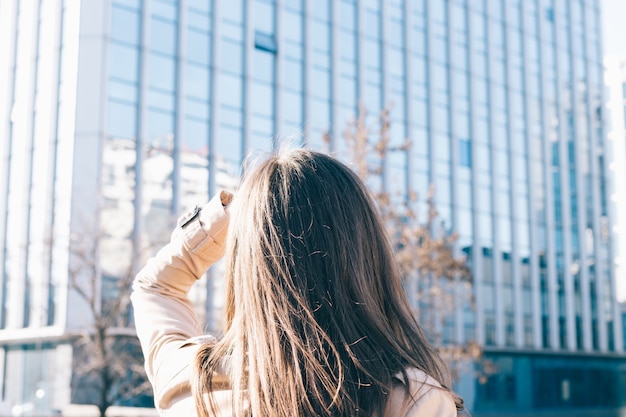 Brunette woman in beige coat looks at the high-rise building